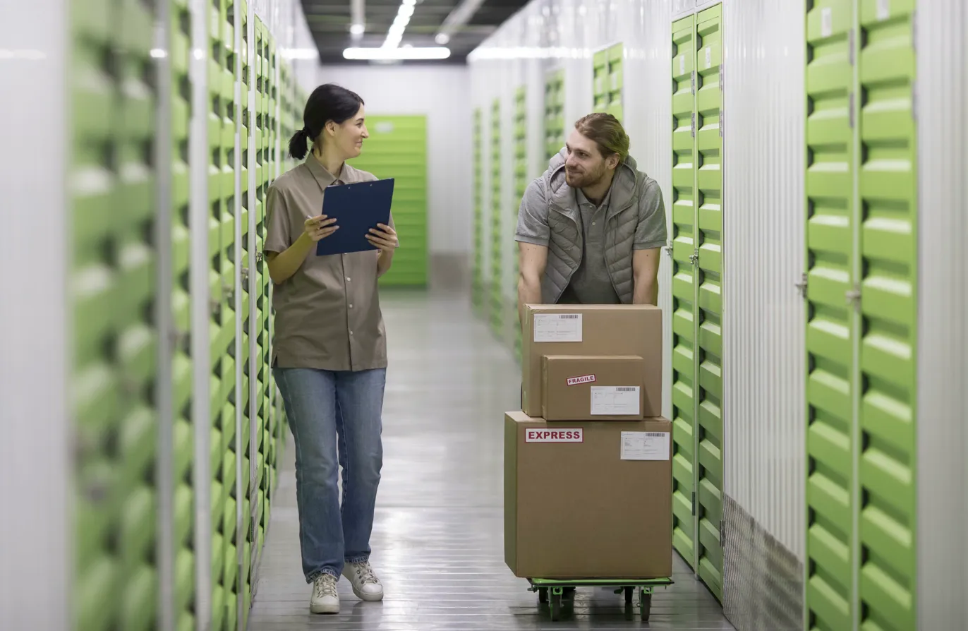 Storage facility staff helping customer with boxes in a clean, modern hallway with green storage units